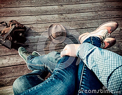 Couple is sitting embracing their legs on wooden floor in sneakers and boots and blue jeans on the outdoors. On the Stock Photo