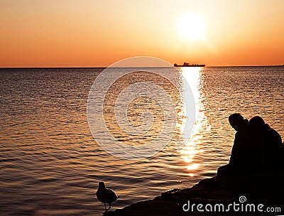 Couple sitting on pier with suggestive view of sea waters at sun Stock Photo