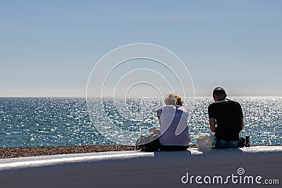 A couple sitting on a wall at the seaside on a summers day enjoying the view of the sea Editorial Stock Photo