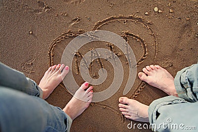 Couple standing on beach with heart and initials in sand Stock Photo