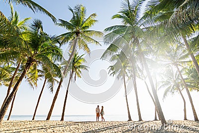 Couple standing on sandy beach among palm trees on sunny morning Stock Photo