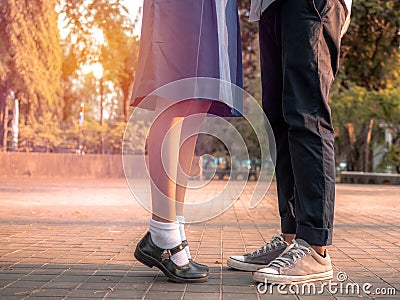 A couple standing together, legs and sneakers of couple in school uniform standing in the park, Symbol sign couple embracing Stock Photo