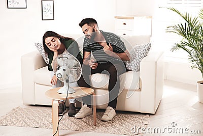 Couple suffering from heat in front of fan at home. Summer season Stock Photo