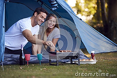 Couple In Tent Camping Sitting By Barbecue Grilling Sausages Stock Photo