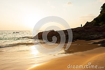 Couple tourists kayaking in tropical sea in the evening. Beautiful golden beach, stone, rocks and waves. Fishermen and sunset sky Stock Photo