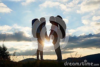 Couple of tourists in love with backpacks facing each other at sunset in the mountains Stock Photo