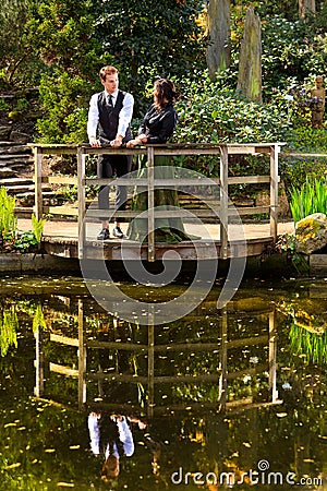 Couple in Victorian fashion near lake with reflections in park Stock Photo