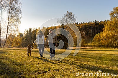 Couple walking dog autumn sunset landscape Stock Photo