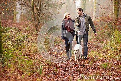 Couple Walking Dog Through Winter Woodland Stock Photo