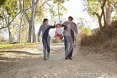 Couple walking on rural path lifting daughter, full length Stock Photo