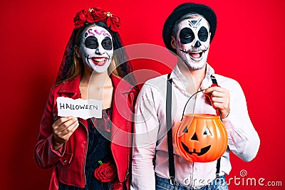 Couple wearing day of the dead costume holding pumpking and halloween paper winking looking at the camera with sexy expression, Stock Photo