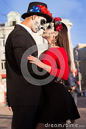 A couple, wearing skull make-up for. All souls day. Boy and girl sugar skull makeup.painted for halloween standing on the street. Stock Photo