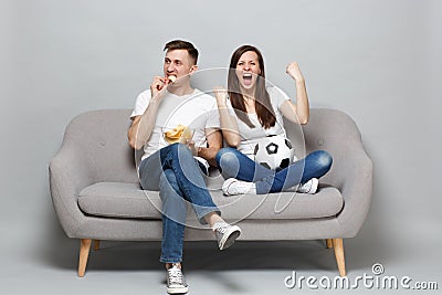 Couple woman man football fans cheer up support favorite team with soccer ball, holding bowl of chips, clenching fists Stock Photo