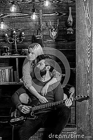 Couple in wooden vintage interior enjoy guitar music. Lady and man with beard on dreamy faces hugs and plays guitar Stock Photo