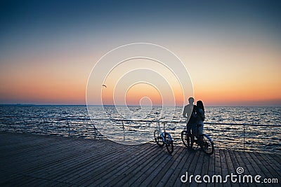 Couple of young hipster lovers hugging at the beach and watching the sunrise at wooden deck summer time Stock Photo