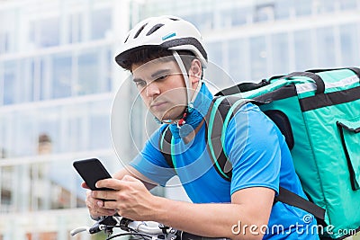 Courier On Bicycle Delivering Food In City Using Mobile Phone Stock Photo