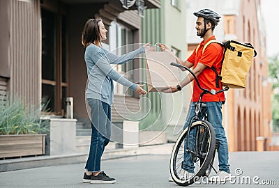 Courier with bicycle delivered shopping bag to client. Smiling girl takes bag from man in helmet with backpack Stock Photo