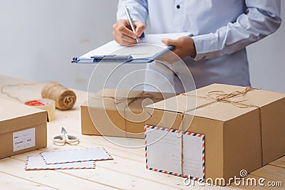 Courier making notes in delivery receipt among parcels at table Stock Photo