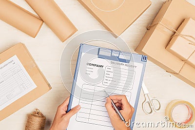 Courier making notes in delivery receipt among parcels at table Stock Photo