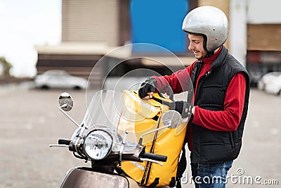Courier On Scooter Opening Yellow Food Delivery Bag Standing Outside Stock Photo