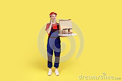 Courier woman holds coffee and boxes with pizza, offers drinks and food delivery, talking via phone. Stock Photo