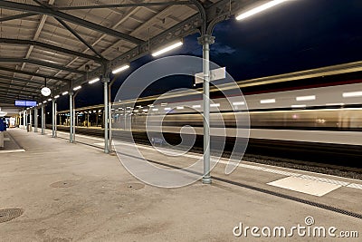 Covered station platform illuminated by led lights. The train passes by at full speed Stock Photo