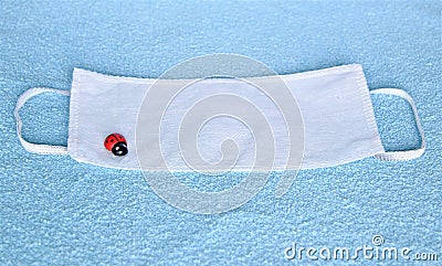 Covid-19 disposable 3-layer white filter mask with lucky charm ladybird, blue towel as a background Stock Photo