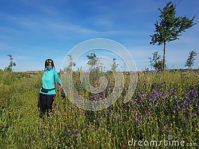 Covid 19 Masked woman contemplates flowers in the field during quarantine Stock Photo