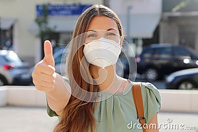 COVID-19 Positive young woman wearing protective mask KN95 FFP2 avoiding Coronavirus disease 2019 showing thumbs up in city street Stock Photo