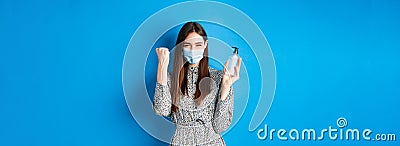 Covid-19, social distancing and healthcare concept. Motivated and excited girl in medical mask cheering, showing bottle Stock Photo
