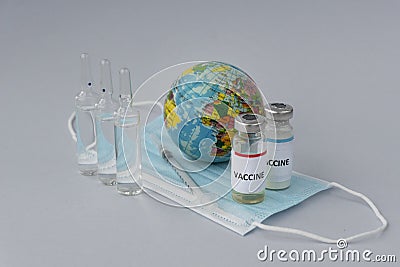 Covid vaccine, syringe for injection and toy globe on medical maski on light background, Stock Photo