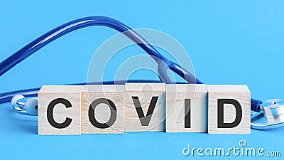 Covid word written on wooden blocks and stethoscope on light blue background Stock Photo