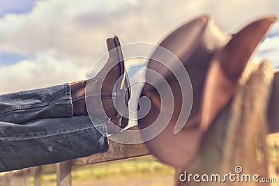 Cowboy boots and hat with feet up on fence resting with legs crossed Stock Photo