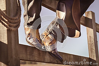Cowboy boots and hat sitting on fence at rodeo stables with feet up resting Stock Photo