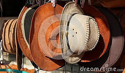 Cowboy Christmas. American West traditional pure leather hats displayed outdoors for sale in sunlight. They are hanging next to Stock Photo