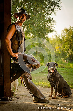 Cowboy stands with dog at the barn. A handsome man with a hat. A sympathetic man. Stock Photo