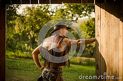 Cowboy stands at the barn. A handsome man with a hat. A sympathetic man. Stock Photo
