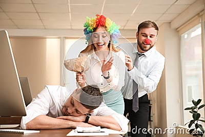 Coworkers popping paper bag behind their sleeping colleague in office. Funny joke Stock Photo