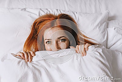coy young woman hiding under bed cover Stock Photo