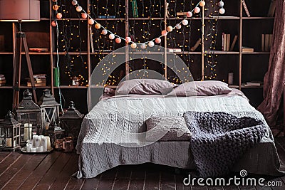 Coziness, comfort, interior and holidays concept - cozy bedroom with bed and garland lights at home. A rack with books Stock Photo