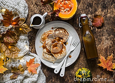 Cozy autumn breakfast still life - pancakes with homemade pumpkin syrup, knitted blanket, maple autumn leaves on a wooden Stock Photo