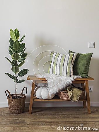 Cozy autumn interior of the hallway - a wooden bench with decorative pillows, a basket with blankets and a homemade ficus flower Stock Photo