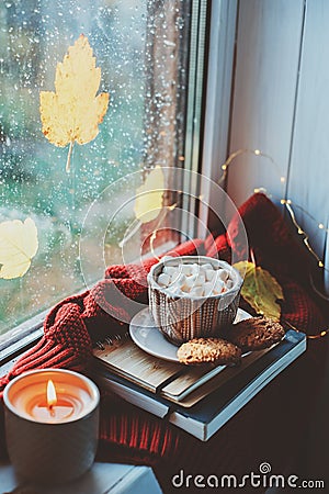 cozy autumn morning at home. Hot cocoa with marshmallows and candle on window in rainy cold day Stock Photo