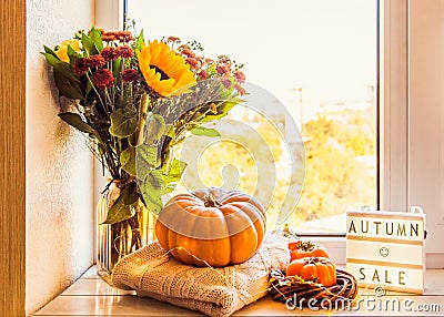 Cozy autumn still life on the windowsill: sunflowers, pumpkin, sweaters, persimmon and lightbox with title Autumn sale Stock Photo