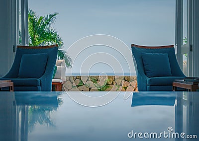 Cozy chairs inside a beach house with open doors leading to palm trees and the ocean Stock Photo