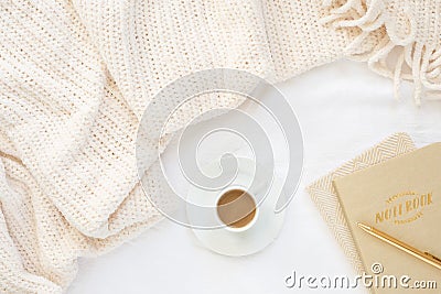 Cozy cream blanket on white bed with gold and natural notebooks, and espresso Stock Photo