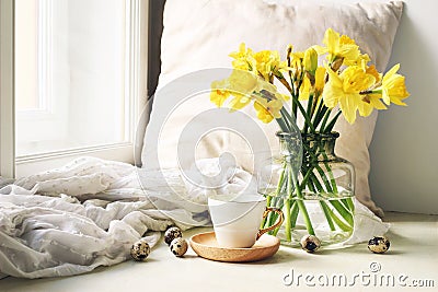 Cozy Easter, spring still life scene. Cup of coffee, wooden plate, quail eggs and vase of flowers on windowsill. Floral Stock Photo