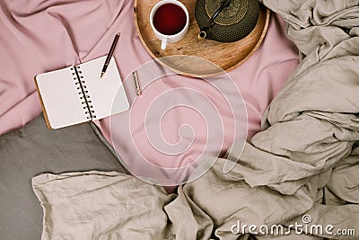 Cozy flatlay of woman`s bed with pink sheets and linen grey blanket with tray and notebook Stock Photo