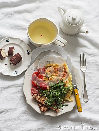 Cozy homemade brunch - omelette with arugula, cherry tomatoes, whole grain toast, green tea, chocolate dessert on a light Stock Photo