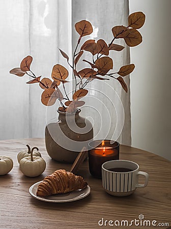 Cozy homemade coffee break. A vase with autumn leaves, a croissant, coffee, a lit candle on a round table in the living room Stock Photo